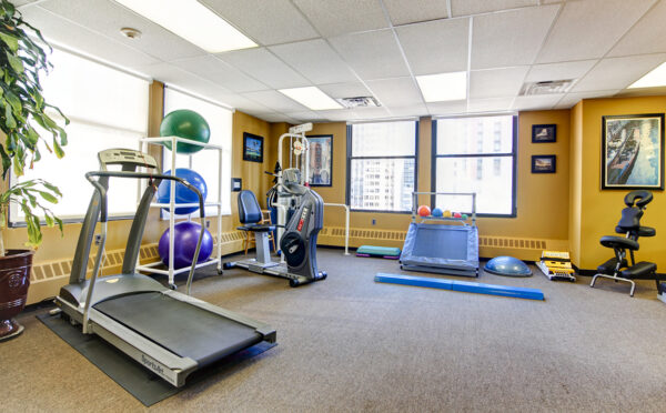 Open rehabilitation gym with a treadmill and conditioning equipment beside tall windows.