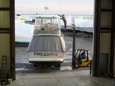 Marine forklift carrying a large powerboat at a boatyard.