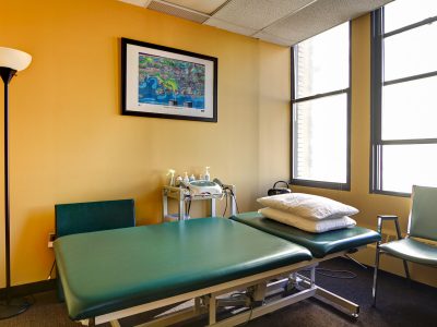 Physical therapy treatment room with a padded table and a decorative wall shelf.