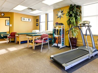 Bright physical therapy gym with exercise equipment, yellow walls, and greenery.