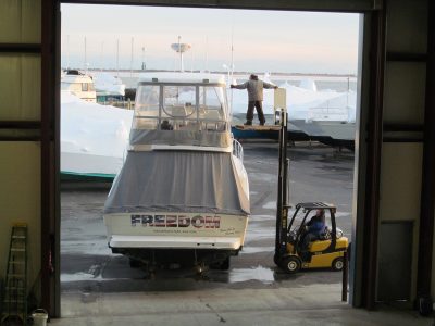Sportfishing boat being moved on a hydraulic trailer outside a marina storage building.