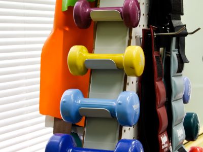 Rack of dumbbells and free weights beside a resistance machine in a physical therapy gym.