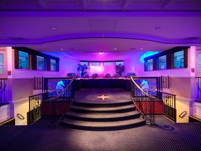 Event hall with a stage, columns, and purple lighting at a waterfront yacht club.