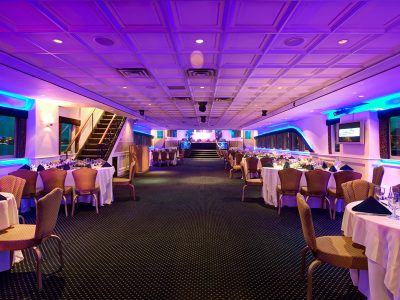 Banquet hall dressed with round tables and purple uplighting for a private event.