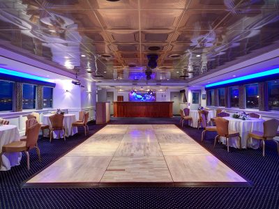 Elegant waterfront banquet hall set with round tables and blue accent lighting for an event.
