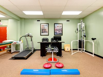 Rehabilitation gym with a treadmill and exercise equipment in a green-walled studio.