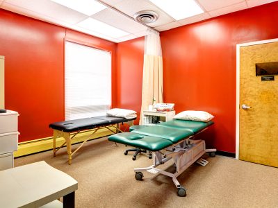 Physical therapy treatment room with a red accent wall and a padded therapy table.