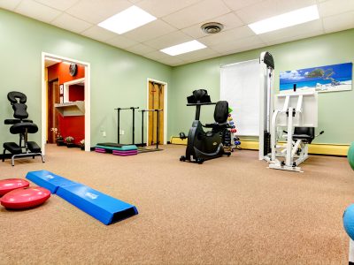 Green-walled physical therapy gym filled with strength and conditioning equipment.