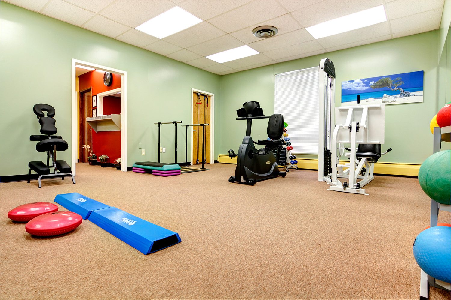 Green-walled physical therapy gym filled with strength and conditioning equipment.
