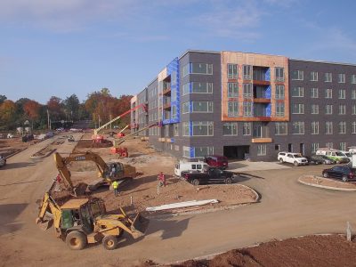 Contemporary multifamily apartment building nearing completion, with parking, crews, and equipment on site.
