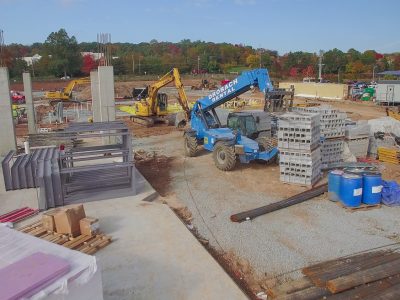 Construction site with a telehandler moving materials beside stacked concrete blocks and building supplies.