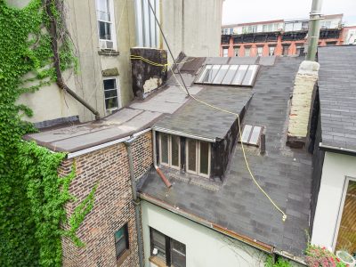 Roof and upper exterior of a historic brick building during renovation, with slate roofing and ivy-covered walls.