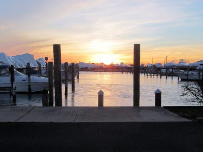 Marina docks and moored boats silhouetted against a sunset over the water.